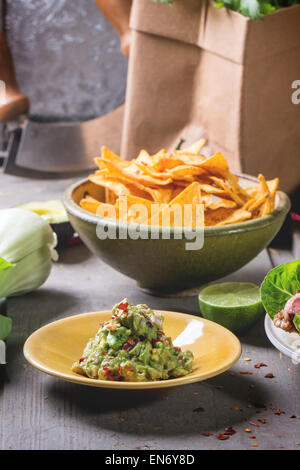 Dîner de style mexicain avec des tacos, des légumes, des nachos chips et guakomole, servie sur table en bois gris. Banque D'Images