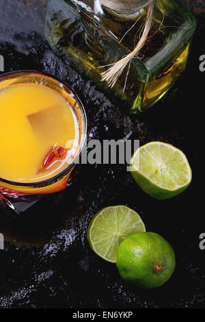 Verre de tequila sunrise cocktail, servi avec une bouteille de tequila anejo tranches de limettes sur fond noir. Faire de la tequila xiang zhang business Banque D'Images