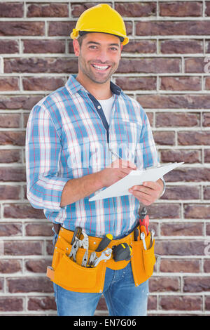 Image composite de portrait of smiling handyman writing on clipboard Banque D'Images