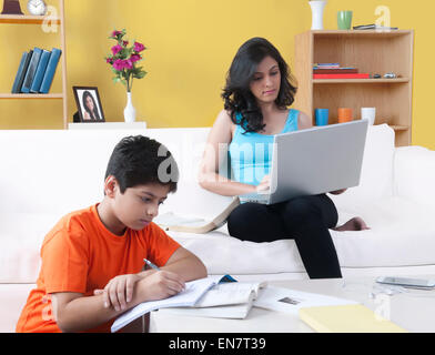 Frère faire ses devoirs alors que sa sœur using laptop Banque D'Images