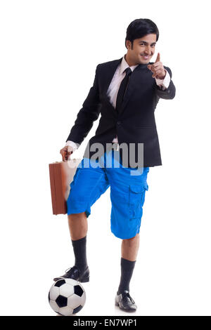 Portrait of smiling young man standing avec ses pieds sur un terrain de football et holding briefcase Banque D'Images