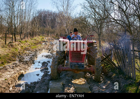 Agriculteur Senior et son petit-fils la conduite d'un tracteur sur une route rurale boueux, rentrant du travail Banque D'Images