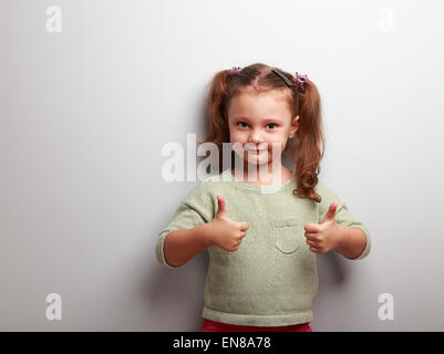 Happy kid girl showing thumb up de deux mains sur fond bleu avec copie espace vide Banque D'Images