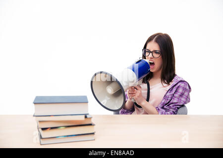 Jeune femme assise à la table et de crier dans un mégaphone sur fond blanc Banque D'Images