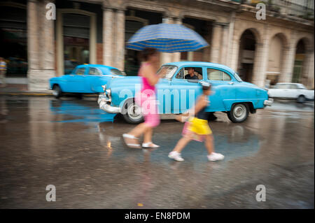 La HAVANE, CUBA - le 13 juin 2011 : la mère et l'enfant à traverser la rue en face de vintage American taxi voiture un jour de pluie. Banque D'Images