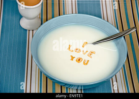 Message d'amour en céréales petit déjeuner bol flottant dans le lait blanc avec cuillère et brown oeuf dur. Banque D'Images