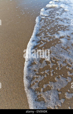 Mousse d'une marée de l'océan sur une plage de sable fin montré comme un arrière-plan vertical Banque D'Images