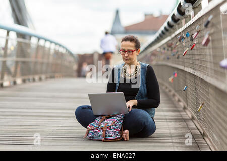 Young woman with laptop assis sur un pont pour piétons dans une vieille ville européenne. Banque D'Images