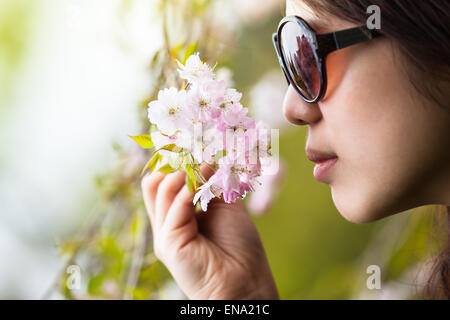 Jeune femme avec les yeux bandés et sentez l'odeur d'une brindille de fleurs de cerisier Banque D'Images