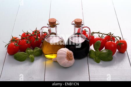 L'huile d'olive et vinaigre dans bouteilles vintage sur table en bois, tomates cerise à l'ail Banque D'Images