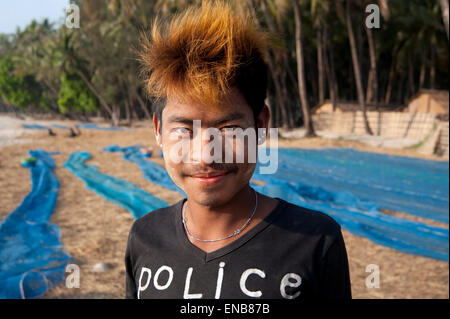 Portrait d'un jeune pêcheur birman funky avec les cheveux teints en bleu sur la plage de Ngapali avec filets de pêche derrière lui Banque D'Images