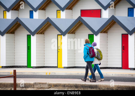 Deux femmes marchant passé nouvelles cabines colorées le long de la promenade à Swanage en mai Banque D'Images