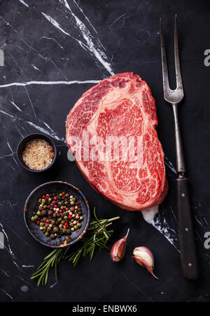 Frais crus de viande marbrée Black Angus Steak Ribeye, les assaisonnements et la viande sur la fourche arrière-plan en marbre noir Banque D'Images