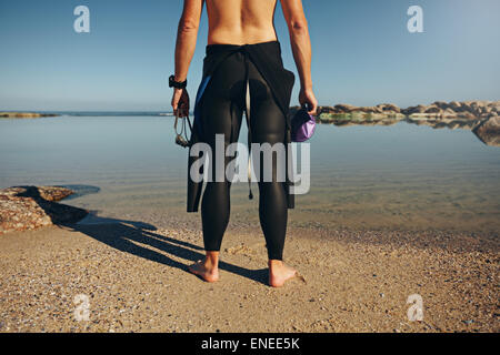 Vue arrière du jeune homme debout sur le lac wearing wetsuit. Cropped shot de triathlète la préparation pour une course de porter une combinaison isothermique pri Banque D'Images