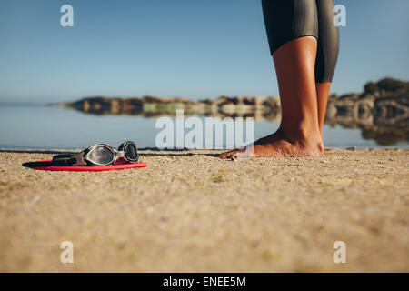 Des lunettes de natation sur le sable aux pieds d'une femme debout par. Se concentrer sur des lunettes. Banque D'Images