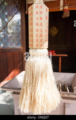 Japon, sanctuaire de Nishinomiya. Le cordage en cloche de chanvre suzu Shinto, et le poids en bois inscrit en rouge de Kanji devant la boîte de collecte saisen-bako. Banque D'Images