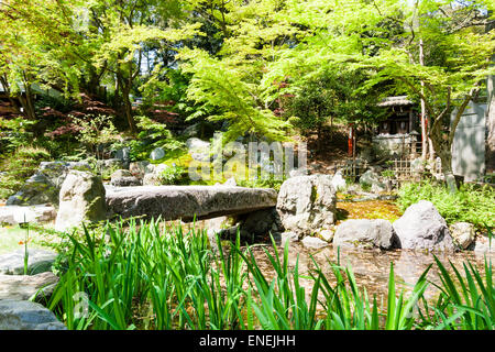 Petit pont en pierre traversant un ruisseau au jardin “Kinkei-en” du sanctuaire tenmangu de Shinto Nagaoka à Kyoto, au Japon, au printemps. Banque D'Images