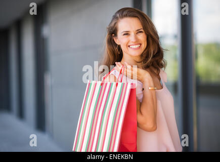 Une femme brune est perçu à partir de la taille vers le haut. Elle est titulaire d'un rayé, multicolore et red shopping le sac sur son épaule droite Banque D'Images