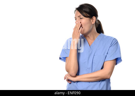 Épuisé belle femme médecin ou infirmière en bleu frotte avec sa main le bâillement permanent à sa bouche d'un long quart de travail fatigant, je Banque D'Images