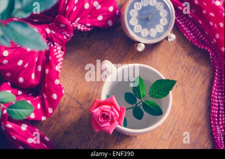 Belles roses frais dans une tasse sur une table en bois et vintage réveil Banque D'Images