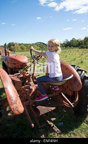 Petite fille jouant sur un vieux tracteur agricole rouge rouillé d'un véhicule de direction de l'enfant Banque D'Images