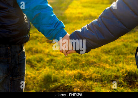 L'amitié pour toujours. Les enfants se tenant la main sur l'herbe verte et du coucher du soleil à l'extérieur. Banque D'Images