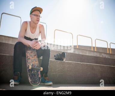 Caucasian man with skateboard sitting on steps Banque D'Images