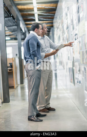 Hommes d'examiner les photographies sur wall in office Banque D'Images