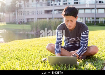 L'homme coréen using laptop in grass Banque D'Images