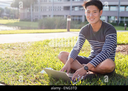 L'homme coréen using laptop in grass Banque D'Images