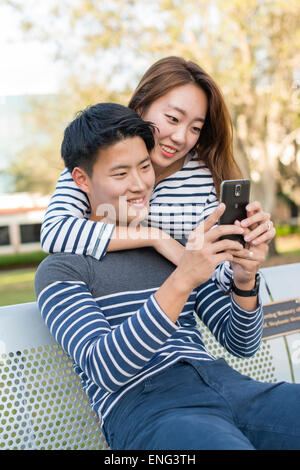 Couple coréen using cell phone in park Banque D'Images