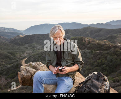 Older Caucasian man using cell phone on rocky hilltop Banque D'Images