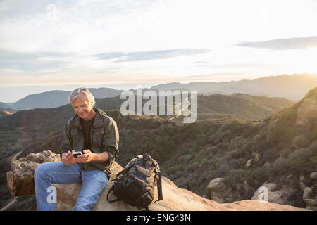 Older Caucasian man using cell phone on rocky hilltop Banque D'Images