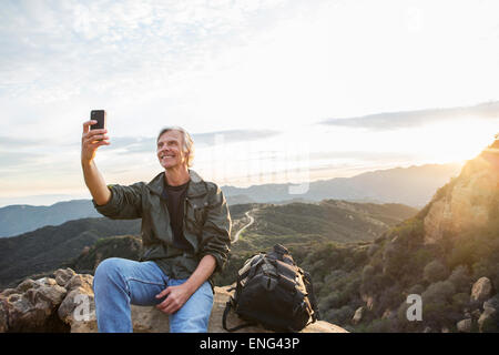 Older Caucasian man taking cell phone photo sur une colline rocheuse Banque D'Images