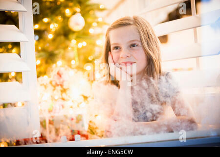 Caucasian girl peering out window à Noël Banque D'Images