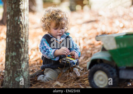 Caucasian boy playing with toy trucks in forest Banque D'Images