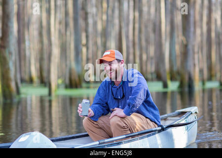 Young man drinking beer en canoë sur la rivière Banque D'Images