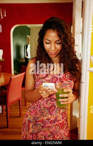 Hispanic woman drinking jus vert et using cell phone Banque D'Images