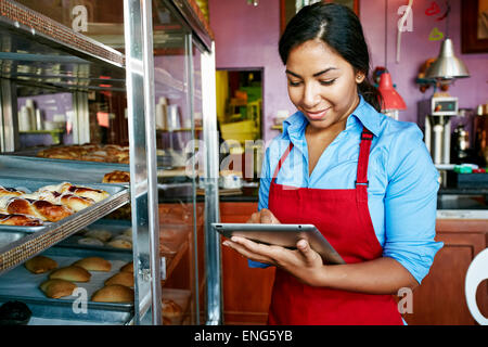 La prise d'inventaire Hispanic waitress with digital tablet in bakery Banque D'Images