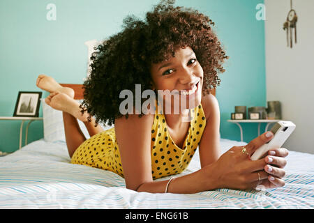 Smiling mixed race woman using cell phone on bed Banque D'Images