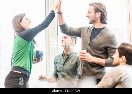 Quatre collègues de travail en pause, de rire et de partage d'une geste high five. Banque D'Images