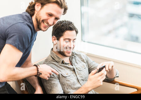 Un homme assis contrôler son téléphone intelligent et un collègue regardant par-dessus son épaule. Banque D'Images