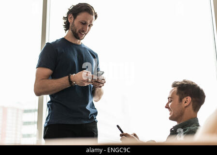 Deux hommes dans un bureau, la vérification de leurs téléphones intelligents. Banque D'Images