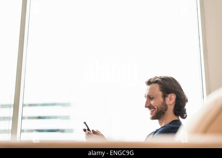 Un homme assis contrôler son téléphone intelligent et rire. Banque D'Images