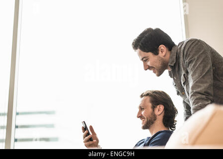 Deux hommes d'affaires à la recherche à un téléphone intelligent et souriant. Banque D'Images