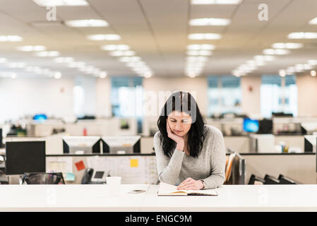 Une femme assise avec sa main posée sur son menton, la lecture d'un livre à un bureau. Banque D'Images