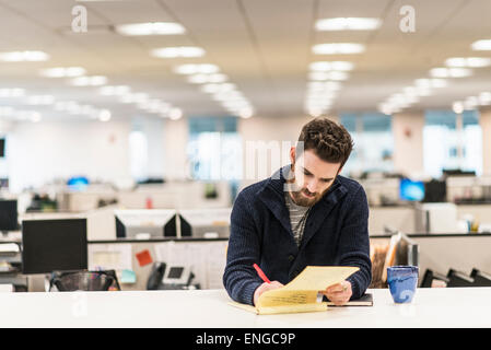 Un homme assis à un bureau dans un bureau écrit avec un stylo rouge. Banque D'Images