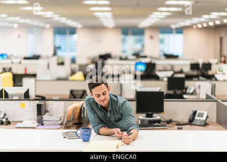 Un jeune homme assis à un bureau dans un bureau avec une plume. Banque D'Images