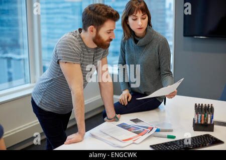 Deux collègues, un homme et une femme à plus de pages imprimées sur un bureau. Banque D'Images