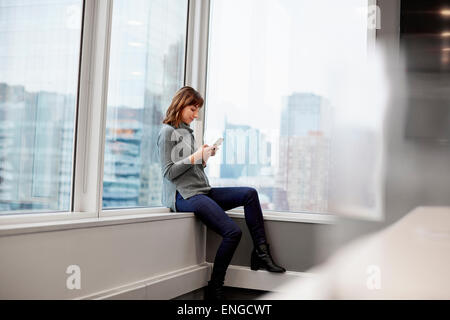 Une femme assise le long, en utilisant un téléphone intelligent. Banque D'Images